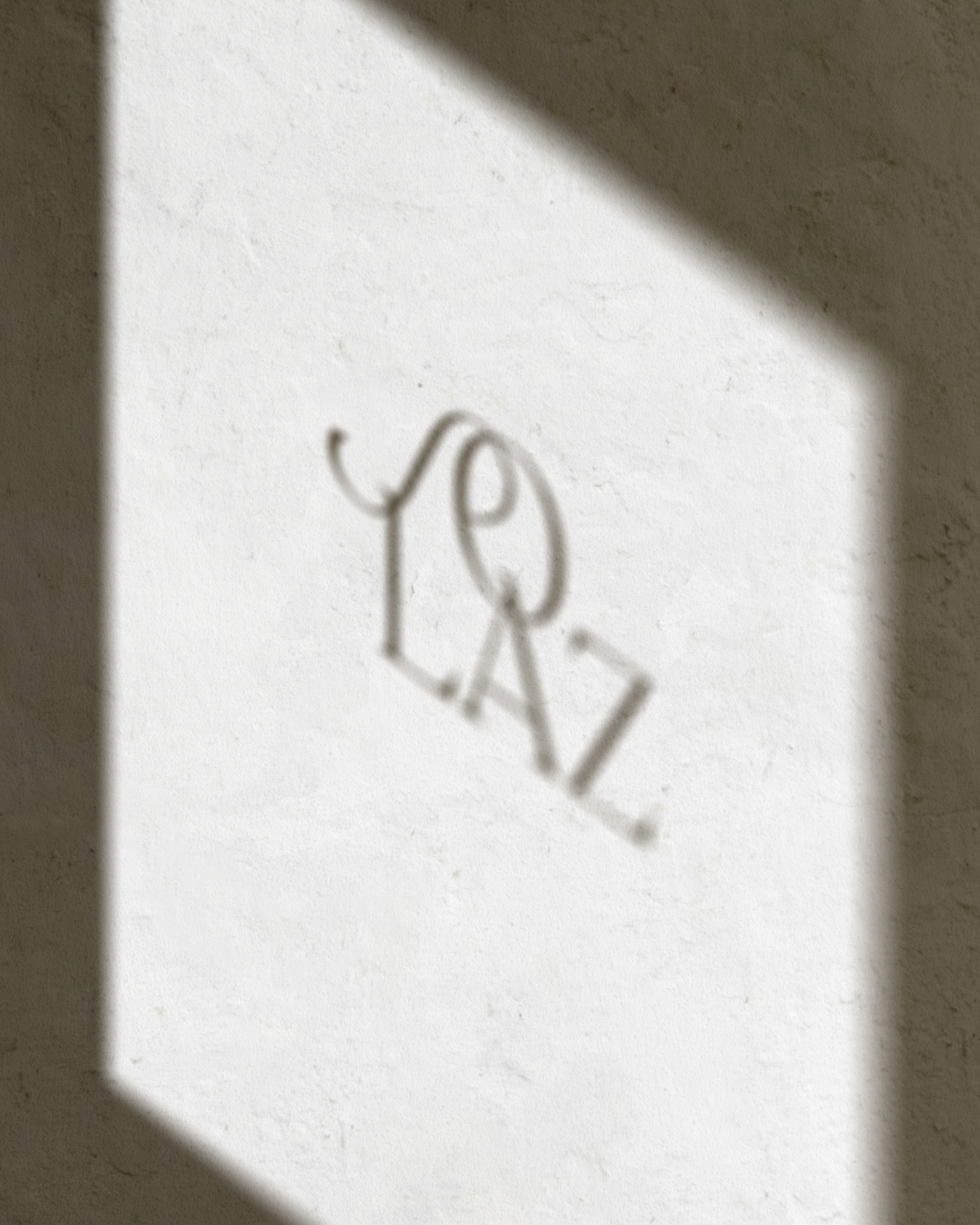 Lumière d’une fenêtre sur un mur enduit, monogramme Solaz en ombre portée